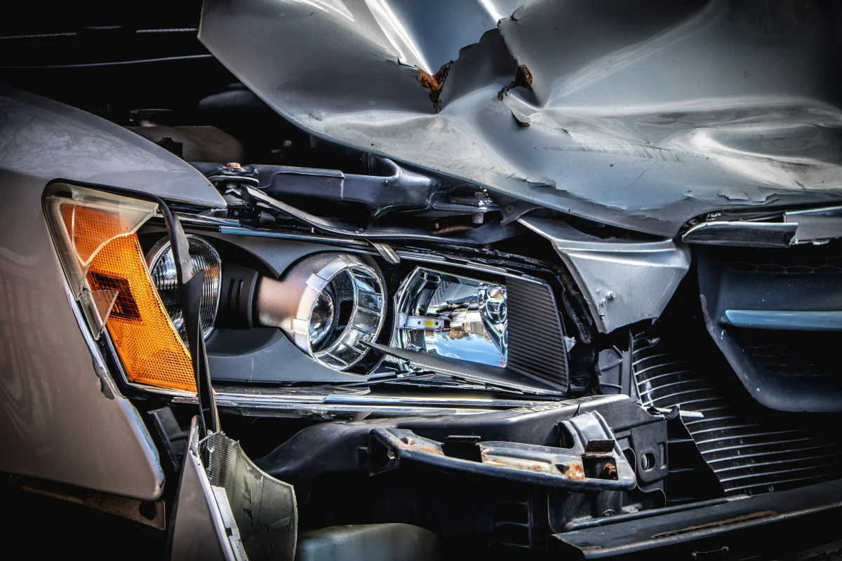 Close-up of a silver car’s damaged hood and headlight.