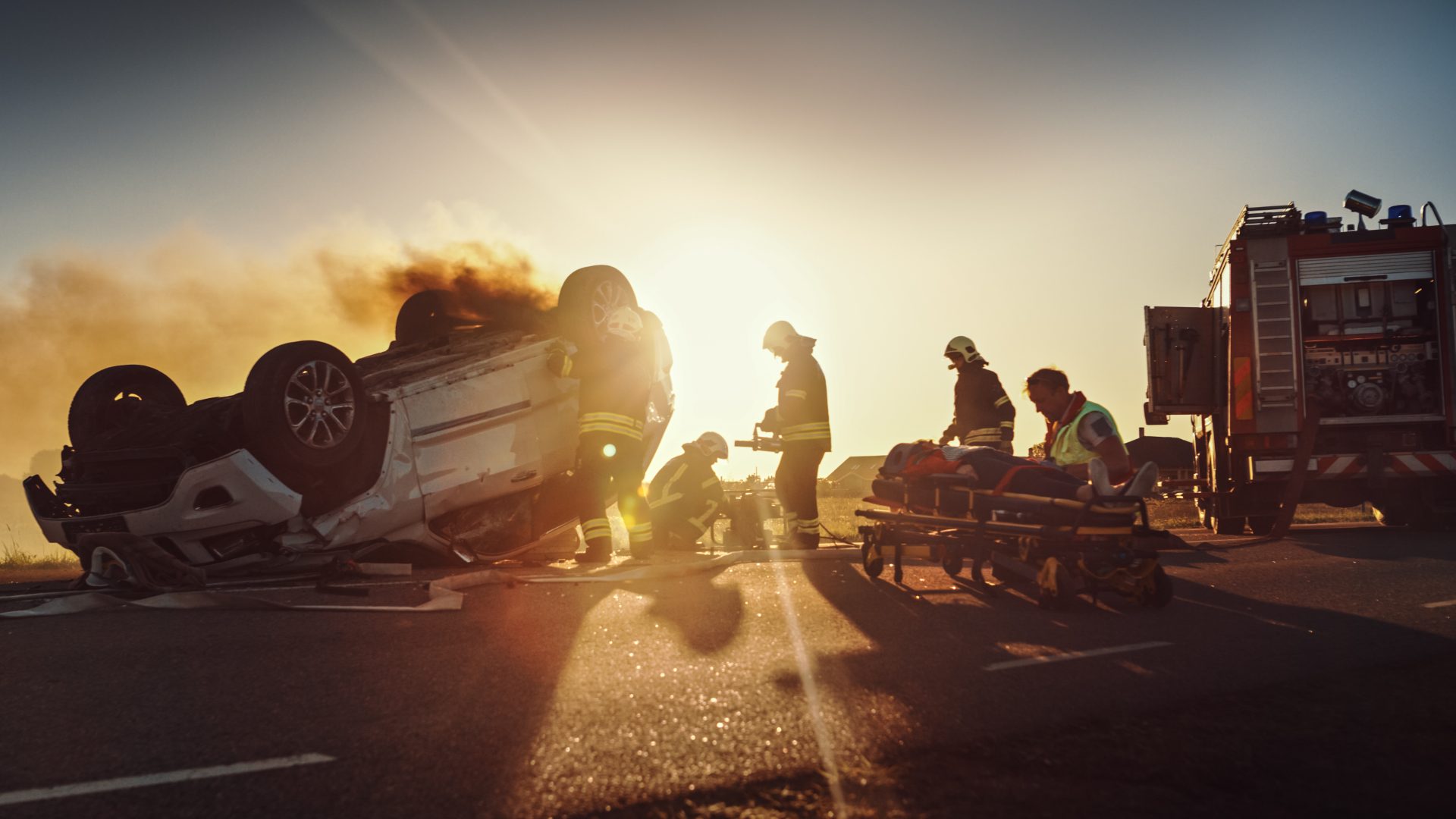Emergency responders assisting at an overturned car on a roadway.